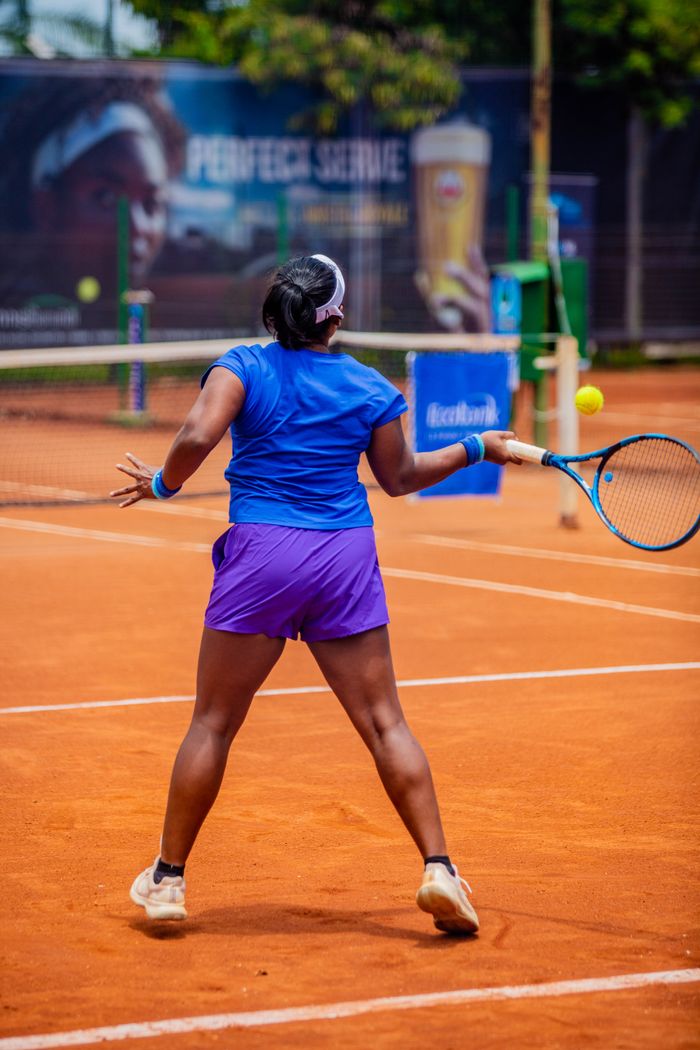 Back view of a female tennis player on a clay court during a sunny day match.